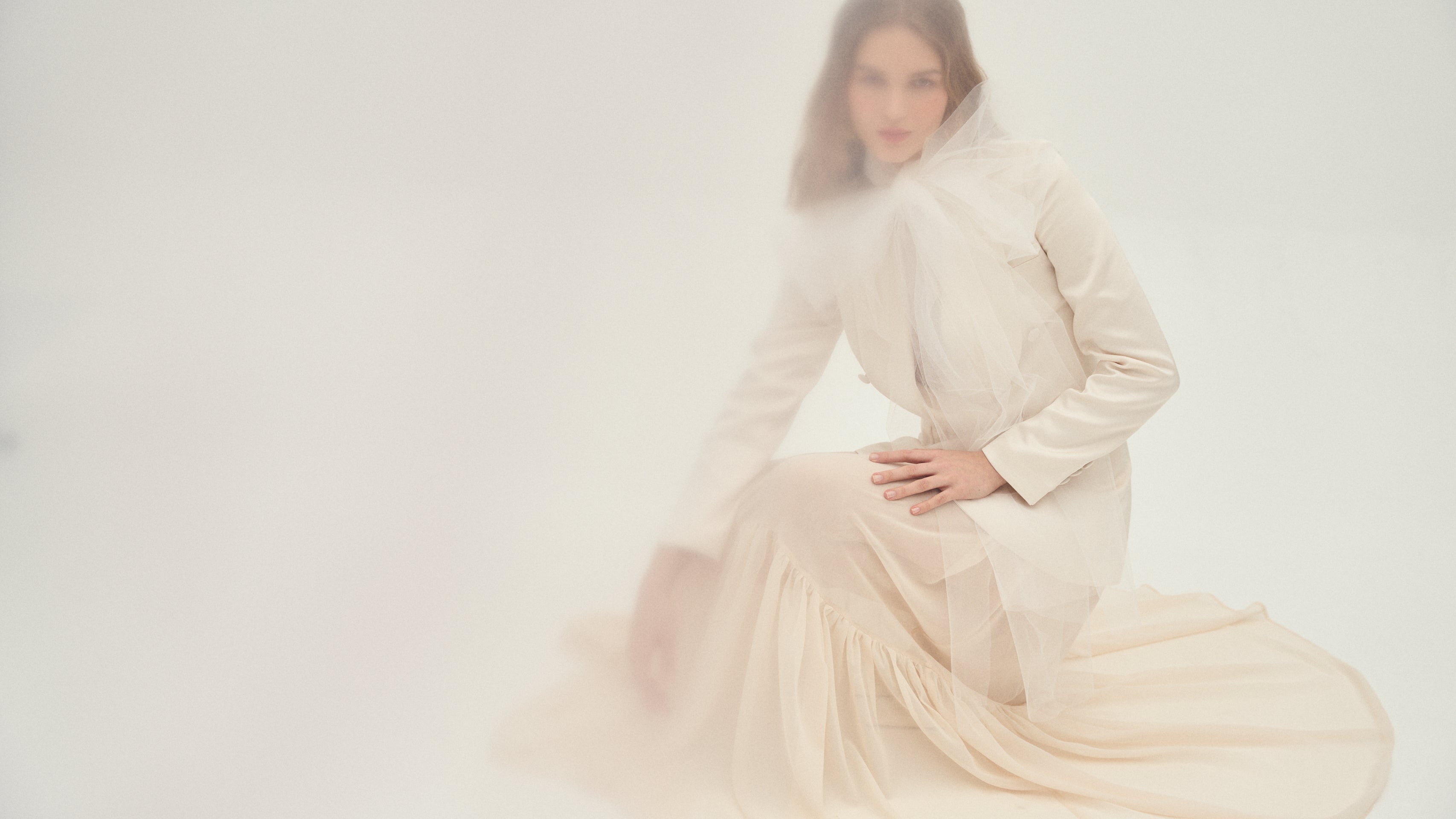 Mujer con vestido y chaqueta de novia posando en un entorno suave para presentar la colección LOVE